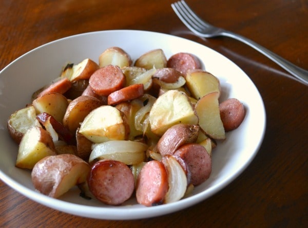 sausage onion and potato sheet pan dinner in a white bowl on a brown table next to a fork