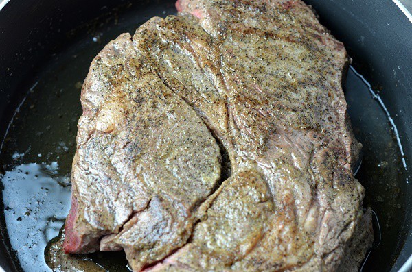 a seasoned pot roast being browned in a pot