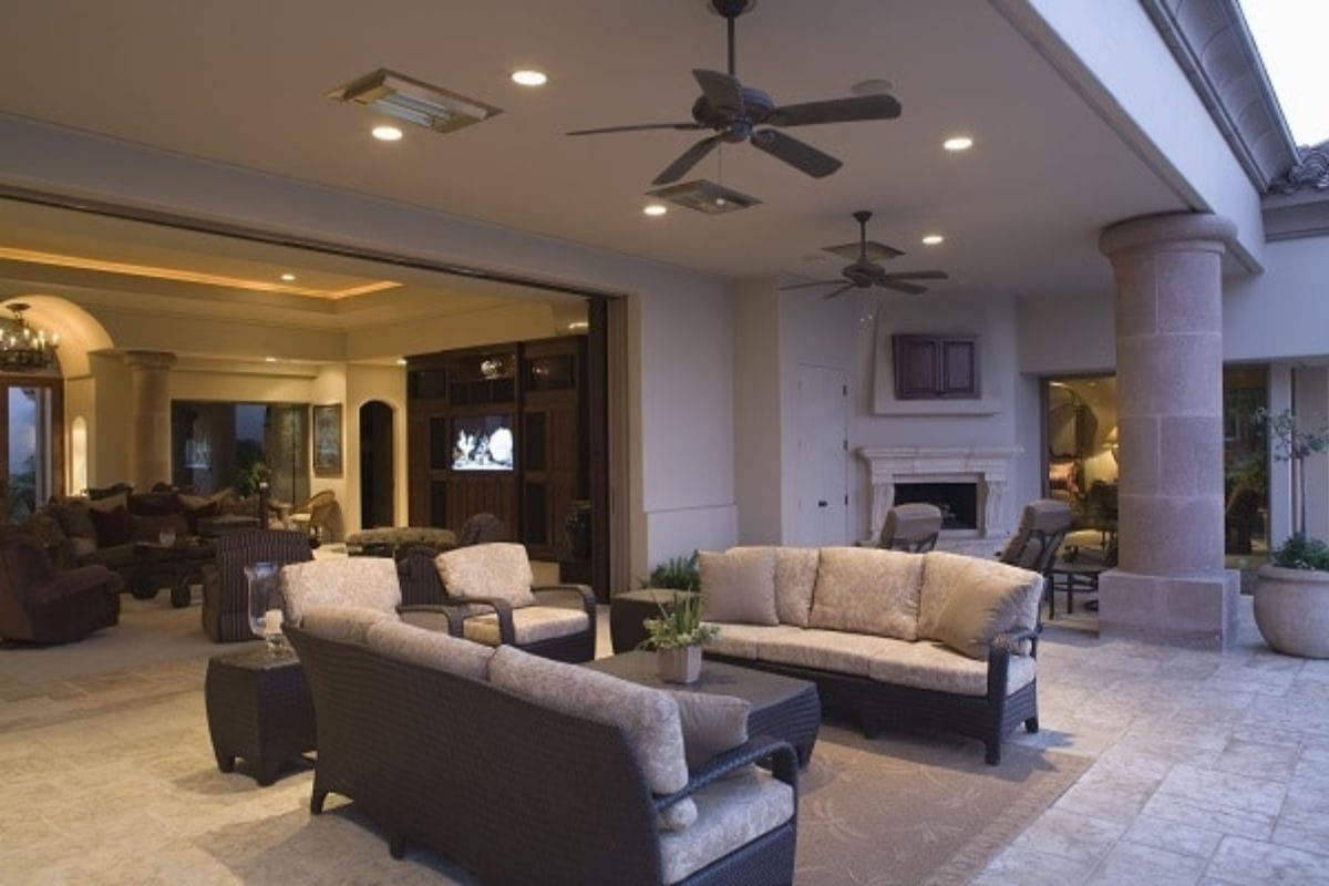Spacious covered patio with wicker furniture, ceiling fans, recessed lighting, and an open view into a furnished living area-perfect for relaxing or trying out new cleaning hacks for moms.