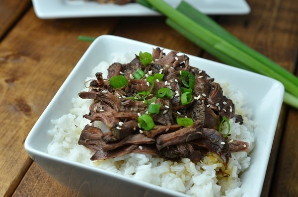 Slow Cooker Asian Pot Roast on rice on a white plate on a brown table next to green onions