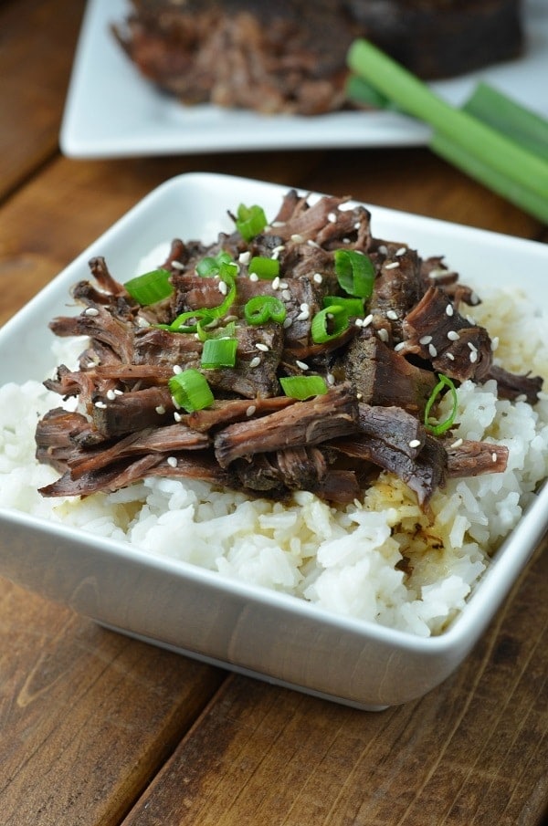 slow cooker asian pot roast and rice in a white dish on a brown table with the rest of the roast on a white plate in the background