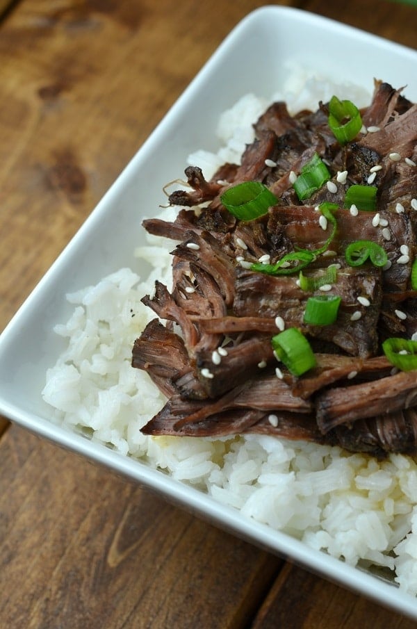 Slow Cooker Asian Pot Roast on rice on a white plate on a brown table