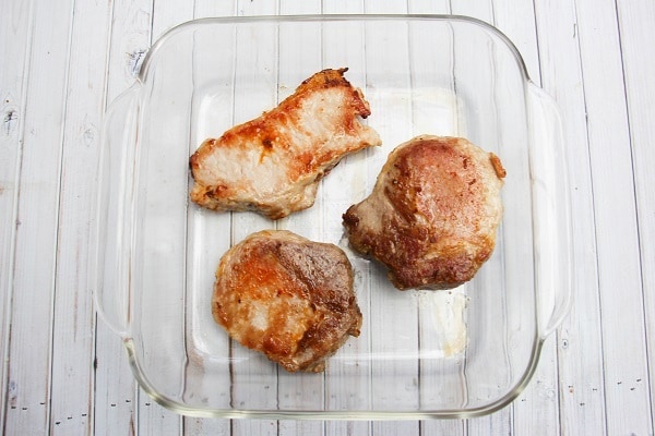cooked pork chops on a glass baking dish on a white wood table