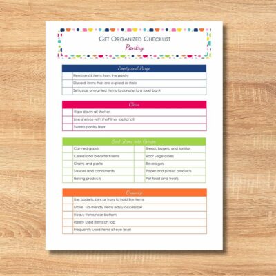 A printed get organized checklist for your pantry rests on a wooden surface, featuring sections for cleaning, shelving, grouping items, and colorful organizing tips boxes.