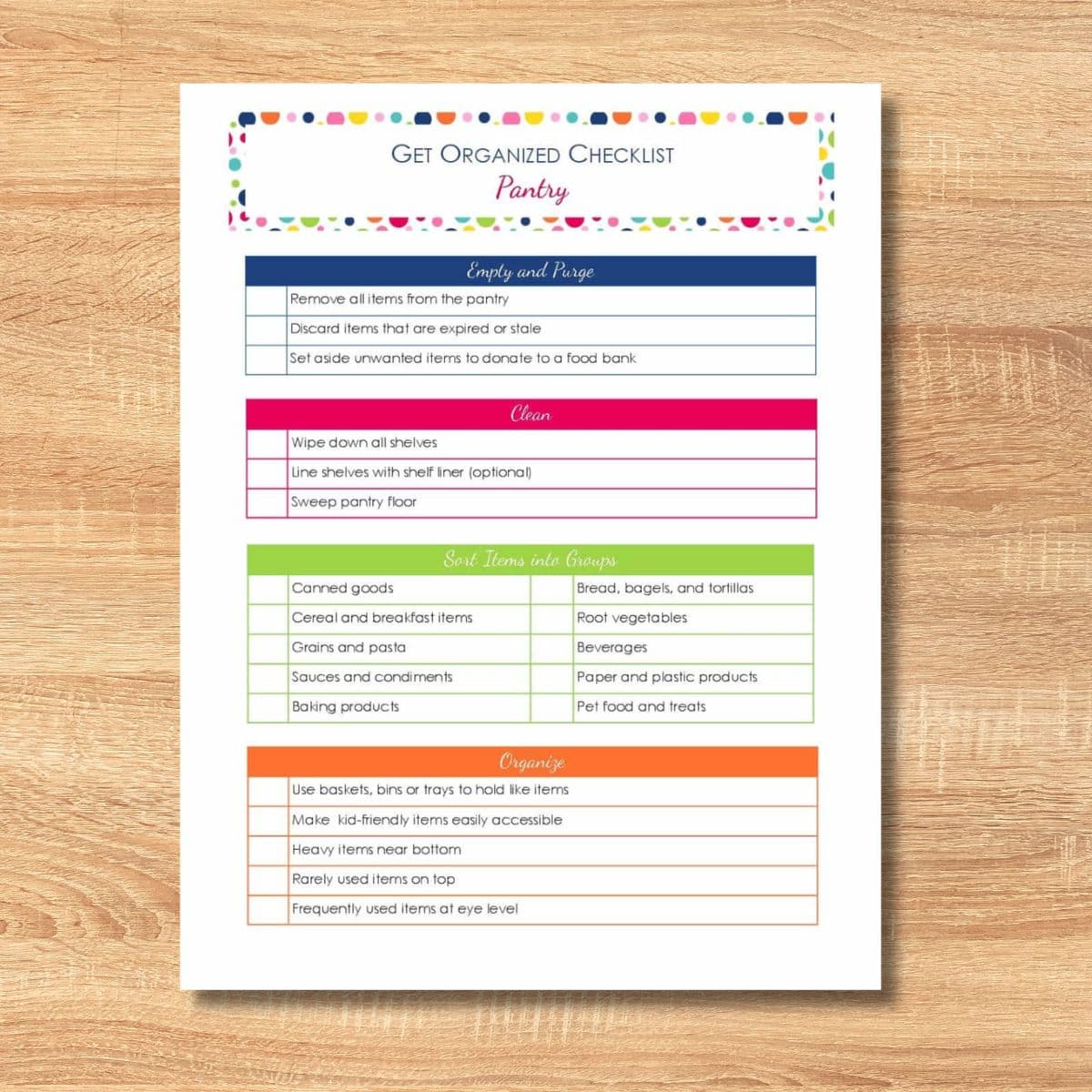 A printed get organized checklist for your pantry rests on a wooden surface, featuring sections for cleaning, shelving, grouping items, and colorful organizing tips boxes.