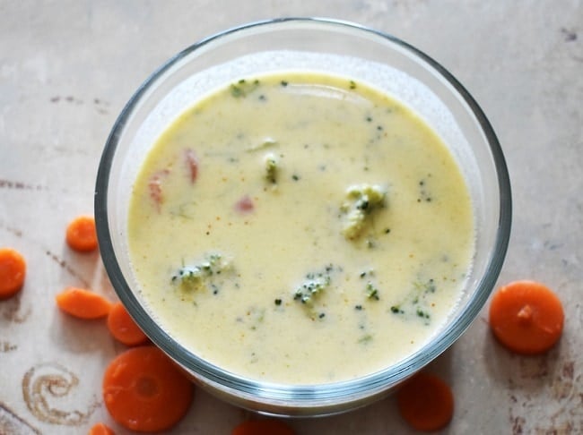 Instant Pot Broccoli Cheese Soup in a bowl next to carrot slices