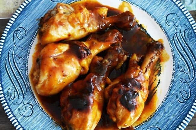 bbq chicken legs and sauce on a white and blue plate