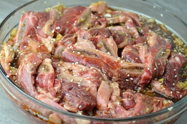 short ribs mixed with marinade and sesame seeds in a glass bowl