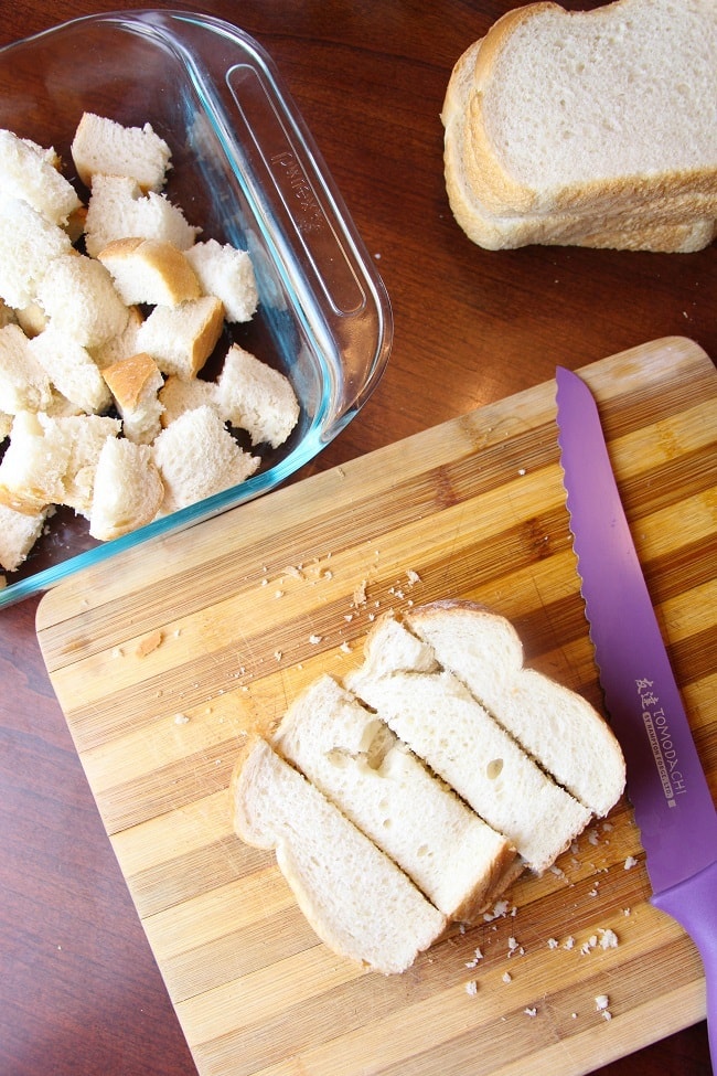 slices of bread in a cutting board next to a purple knife with more slices of bread and a dish of cubed bread in the background