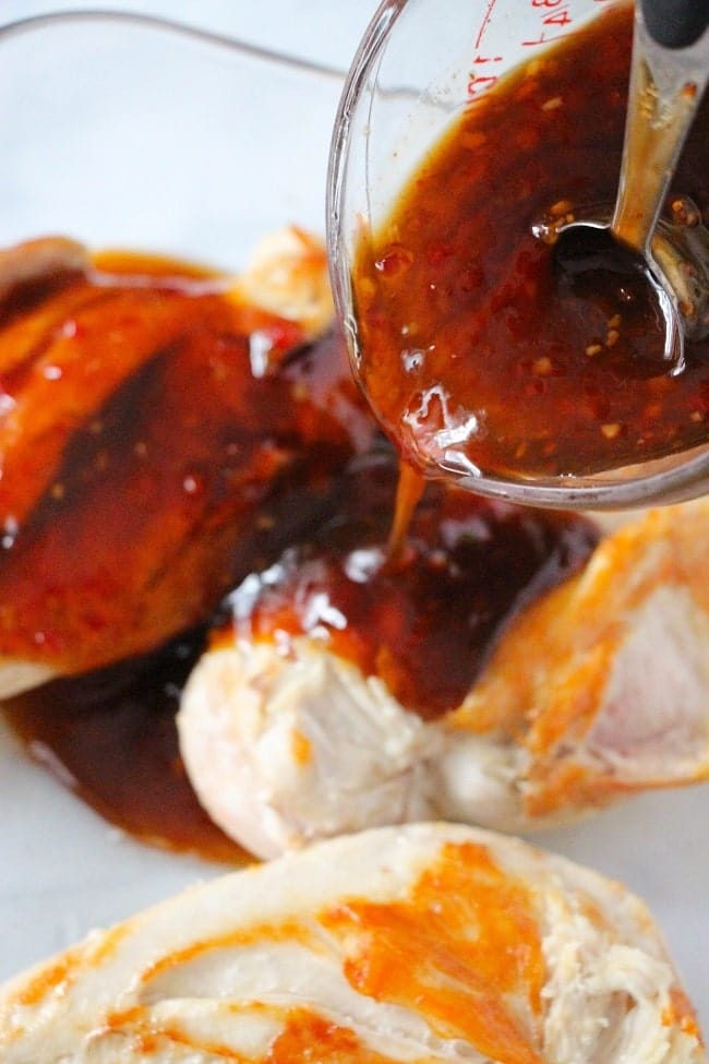 sauce being poured from a glass measuring cup onto chicken breasts in a glass baking dish
