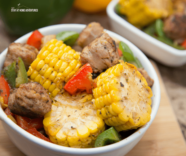 a white bowl filled with sausage, corn on the cob and green and red peppers with another bowl in the background