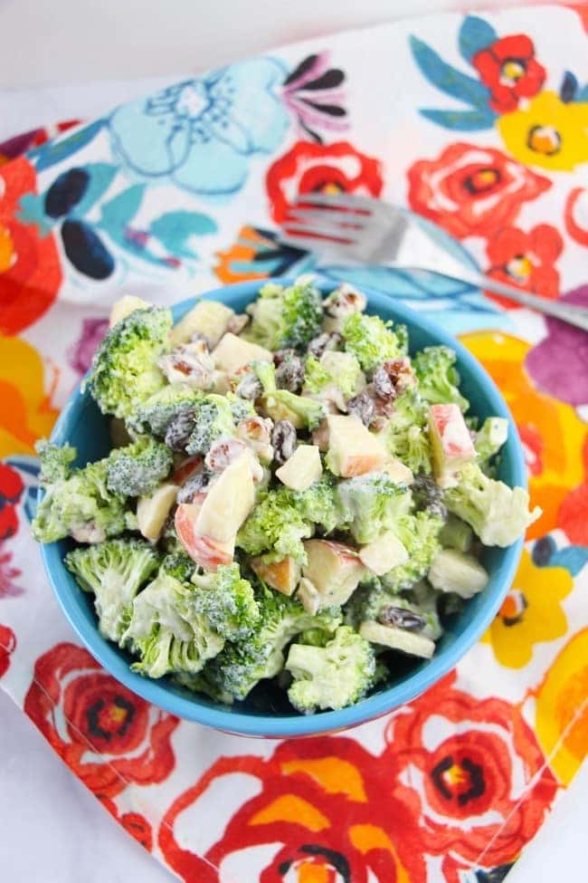 broccoli salad in a blue bowl on a floral linen with a fork next to it