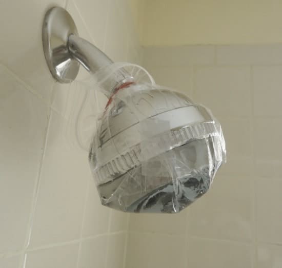 a shower head with distilled vinegar in a plastic bag wrapped around it