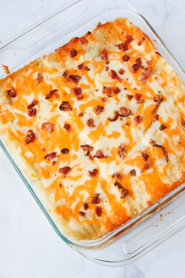 lasagna topped with cheese and bacon in a glass dish on a white counter