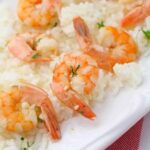 Cooked shrimp with tails on served over a bed of white rice, garnished with small pieces of green herbs on a white plate—perfect for an easy instant pot shrimp scampi dinner.