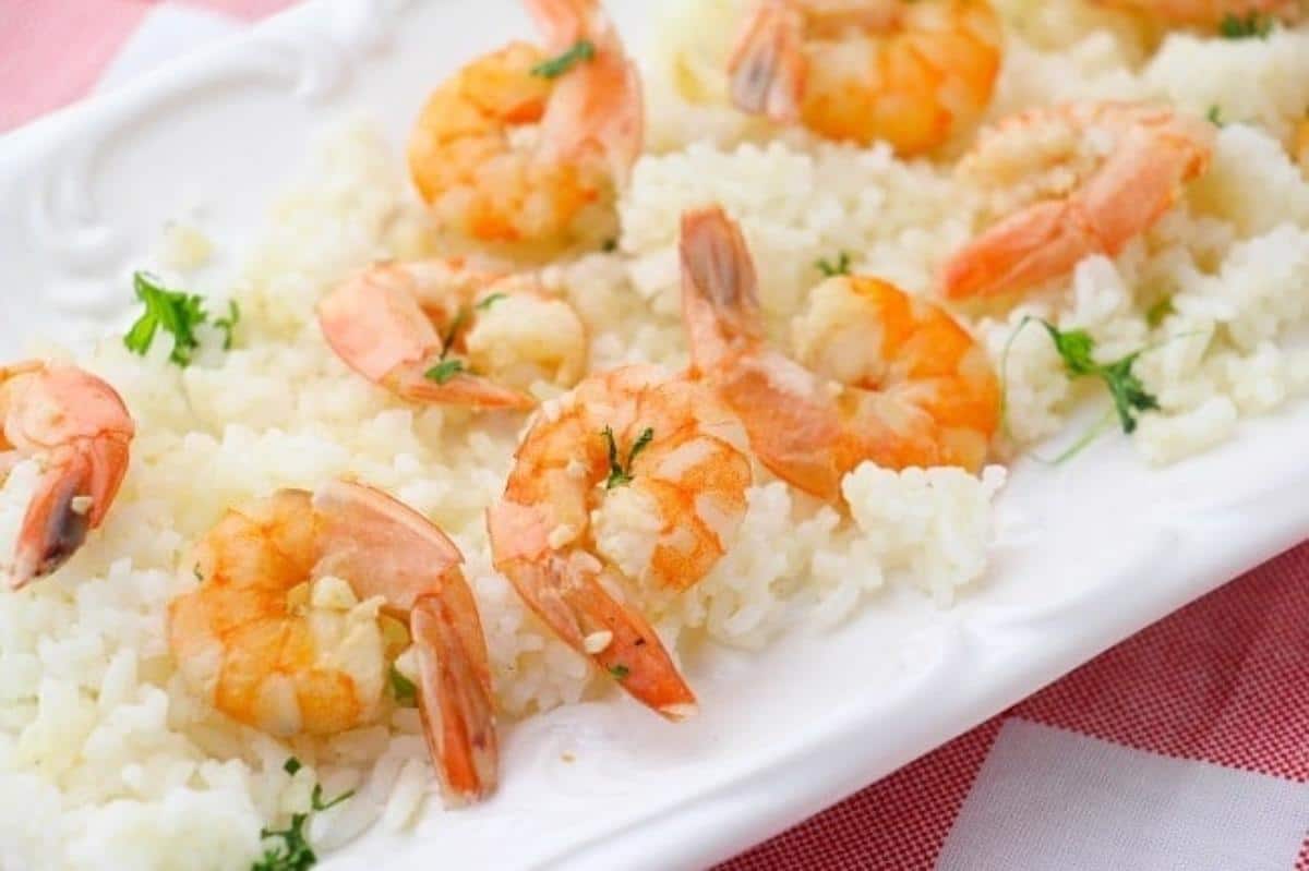 Shrimp scampi with rice on a white plate on a red and white checkered cloth.