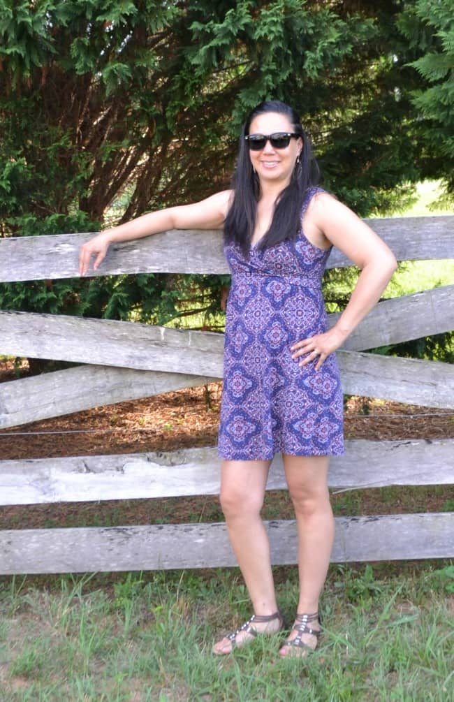 a woman wearing a dress, sunglasses and sandals while standing next to a fence outside