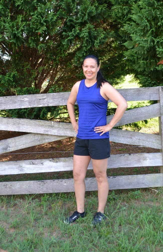 a woman wearing a tank top, shorts and tennis shoes standing next to a fence outside