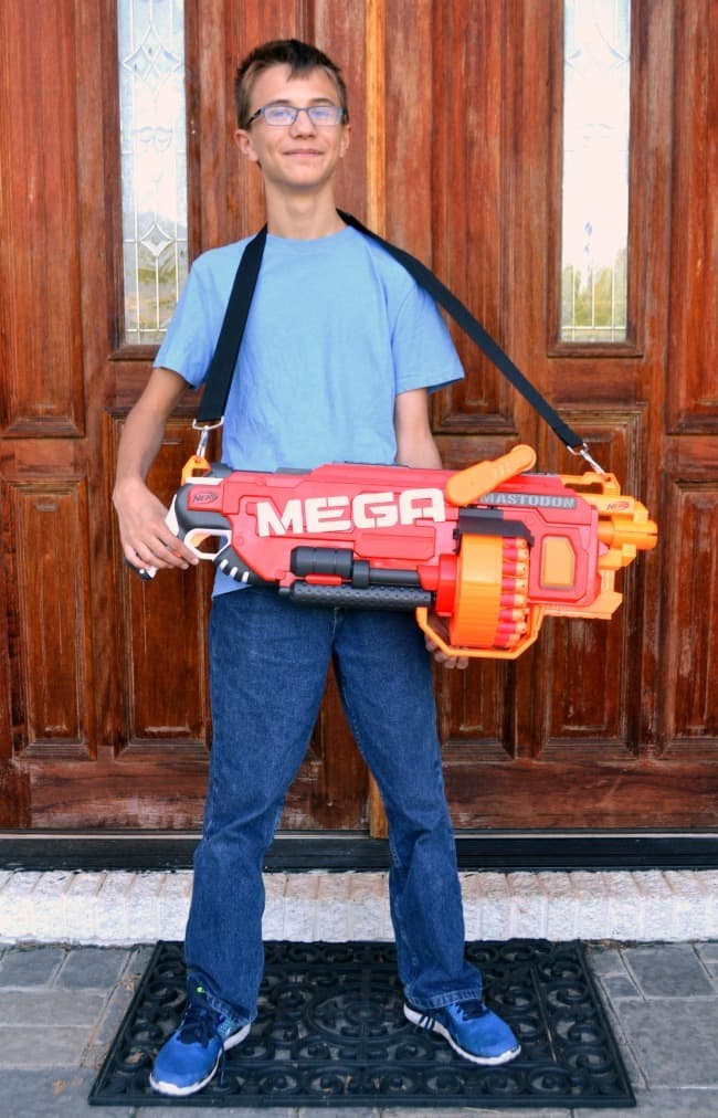a boy standing holding the nerf megadon blaster on his front porch