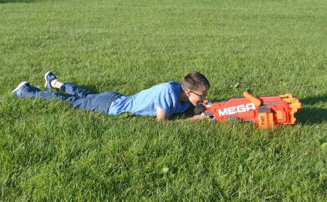 a boy laying in the grass with playing with the nerf megadon blaster