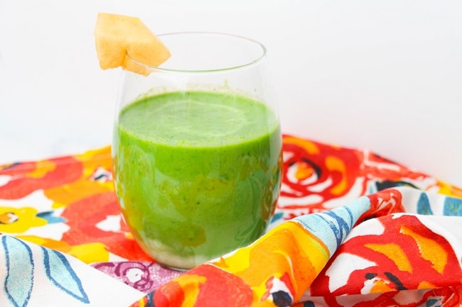 a cantaloupe green smoothie with a wedge of cantaloupe on the side on the side of the glass on a flowered cloth