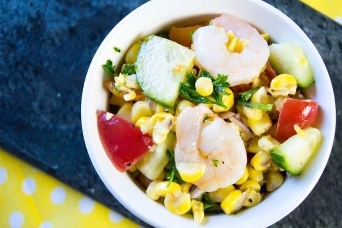 Grilled corn salad topped with shrimp in a white bowl on a blue and yellow cloth.