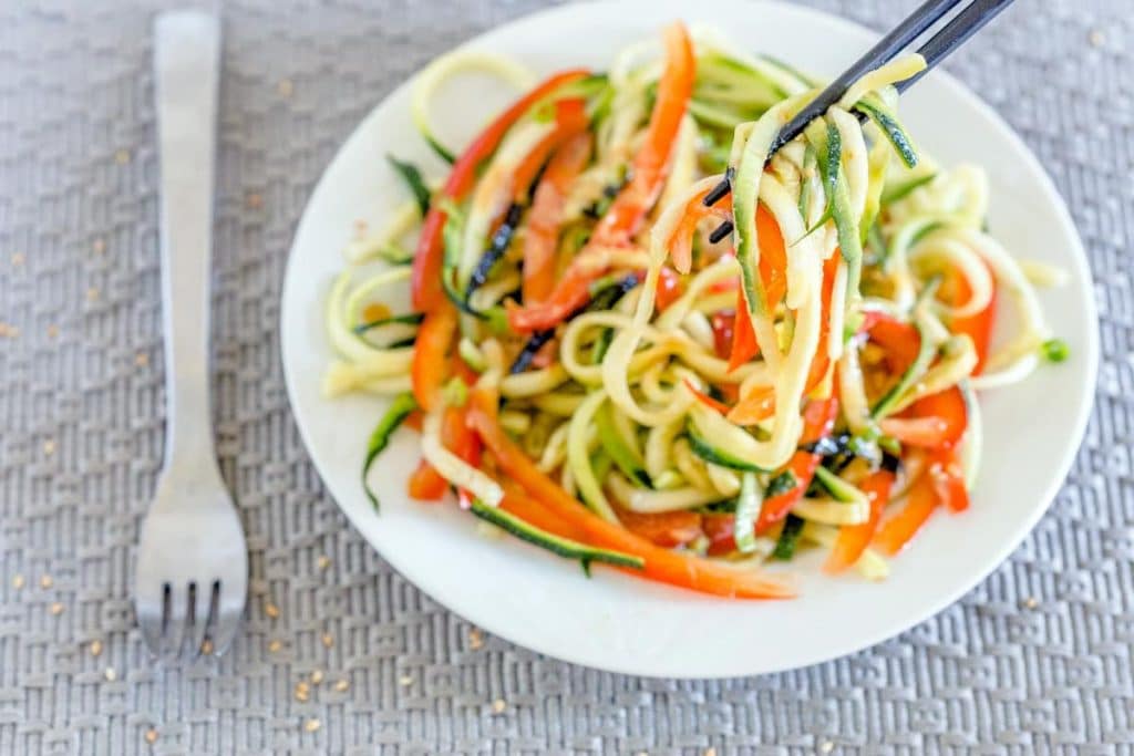 Japanese Zucchini Noodle Salad with Miso Dressing with on a plate with chopsticks lifting some up, next to a fork on a gray cloth