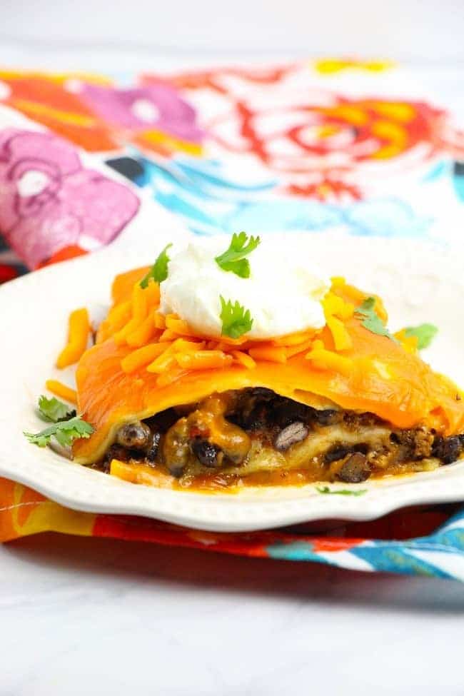 taco lasagna topped with sour cream and parsley on a white plate on a colorful flowered cloth