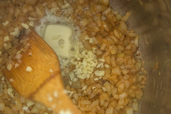 risotto, onion, garlic and butter cooking in an instant pot with a wooden spoon
