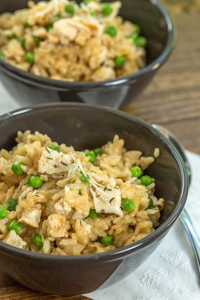 Instant pot chicken and pea risotto in two black bowls on a wood table