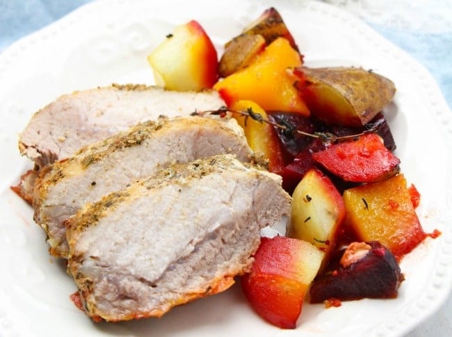 sliced roasted garlic and herb pork loin next to vegetables on a white plate