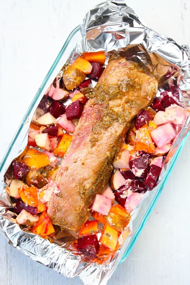 roasted garlic and herb pork loin, potatoes, beets and squash in a glass baking dish lined with foil, on a white table