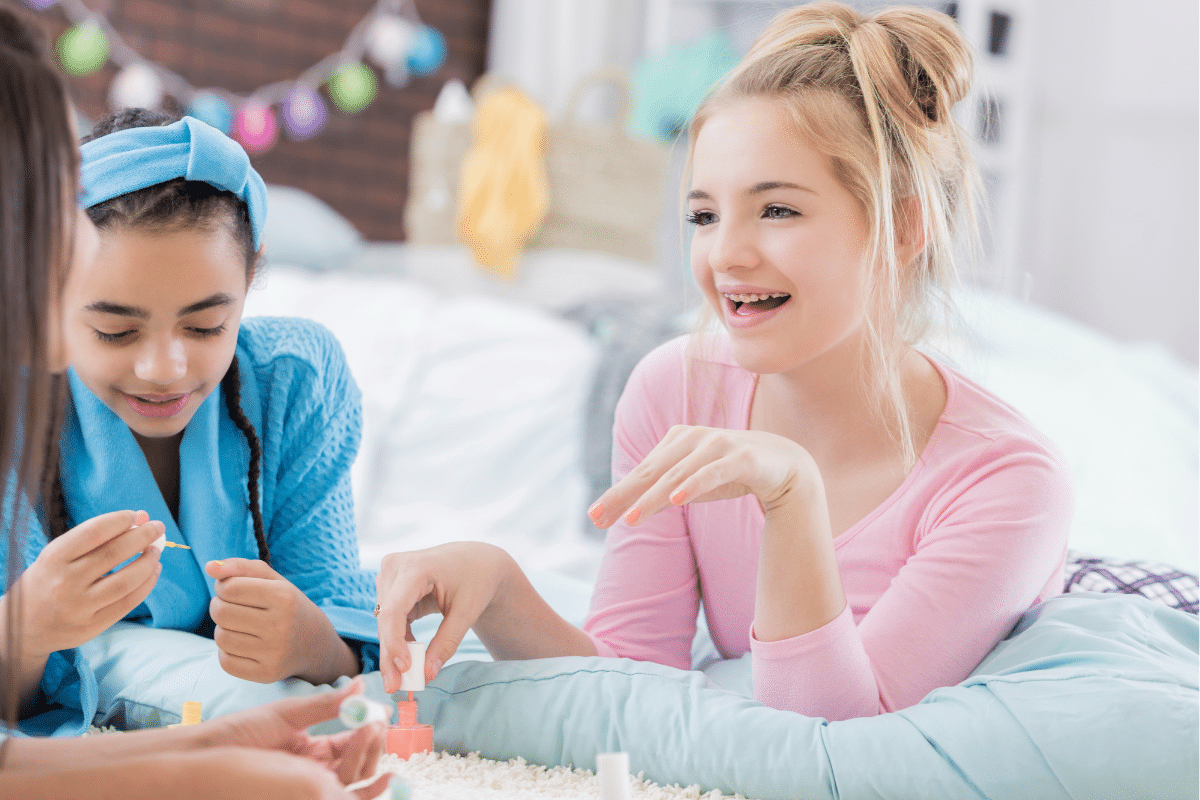 Three girls doing manicures on the bed.