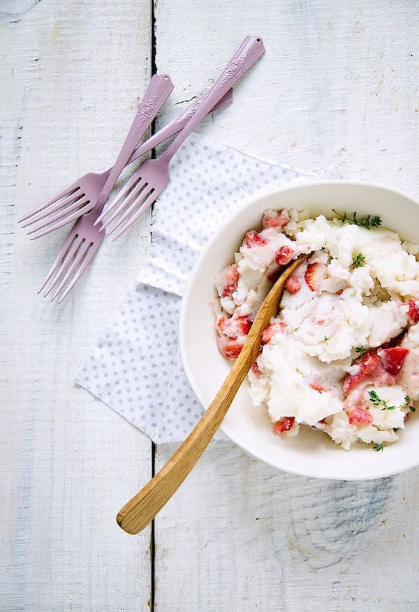 strawberry mashed potatoes in a white bowl with a wooden spoon next to three pink forks on a white wood table
