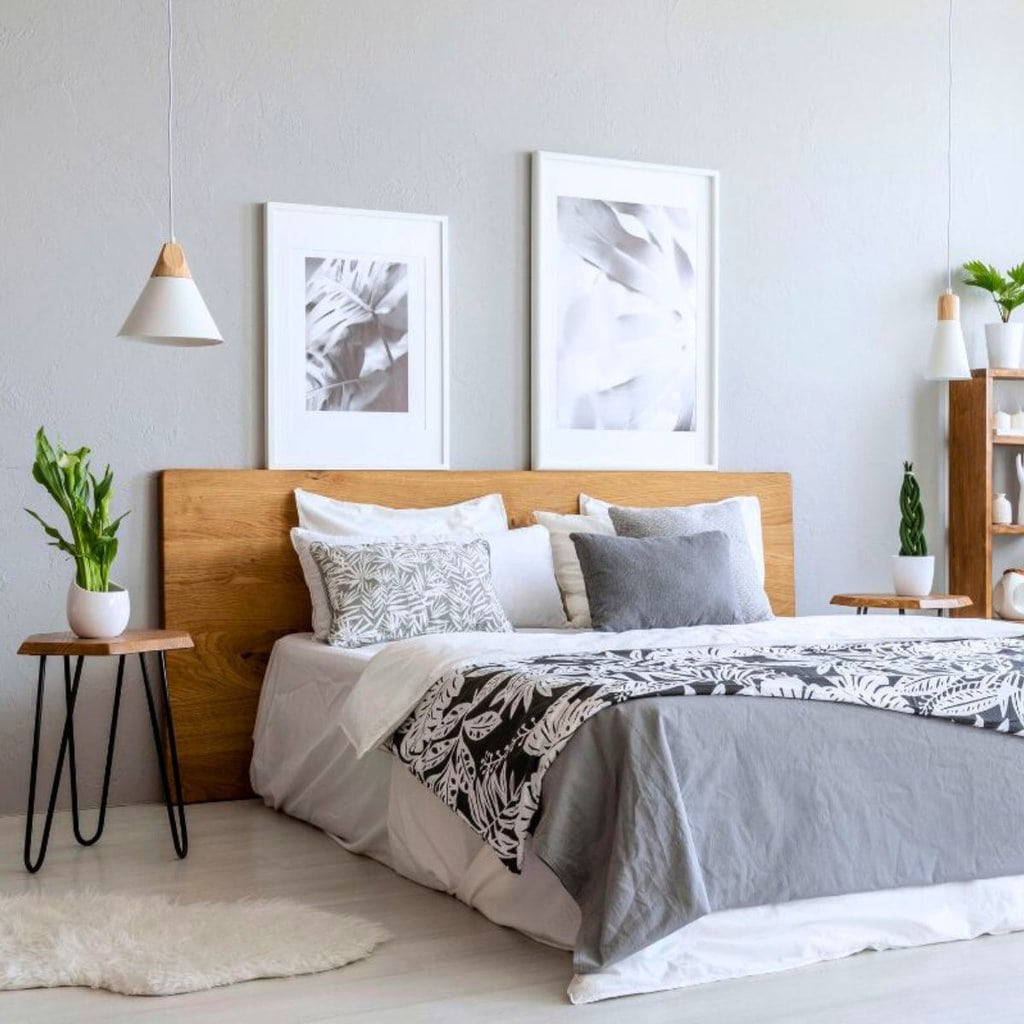 A modern bedroom with a wooden headboard, gray and white bedding, framed wall art, potted plants, and minimalistic decor—perfect to freshen up your bedroom with a stylish and serene atmosphere.