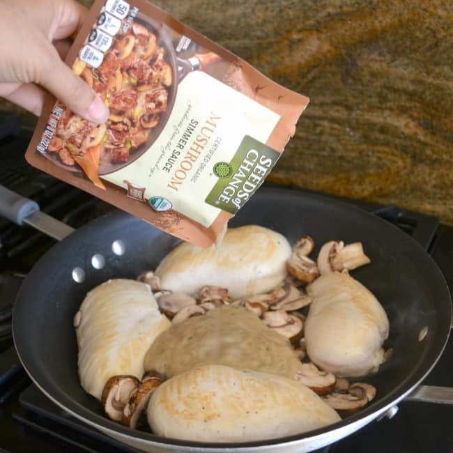 mushroom sauce being poured into a pan of chicken and mushrooms