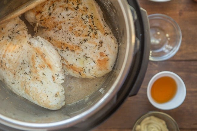 chicken being cooked in an instant pot next to bowls of honey and mustard on a brown table