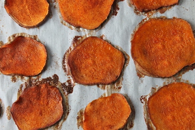 sliced sweet potatoes coated with cinnamon sugar on parchment paper on a baking sheet
