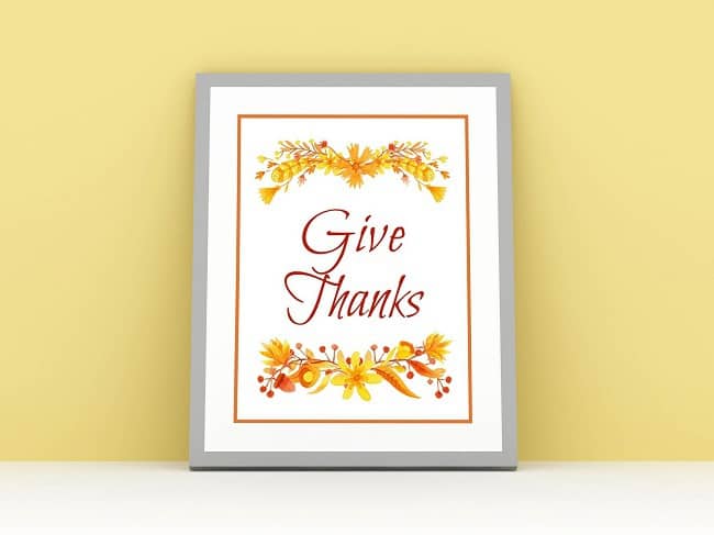 a printable with text reading Give Thanks with Fall flowers and leaves on top and below, in a gray frame on a yellow background