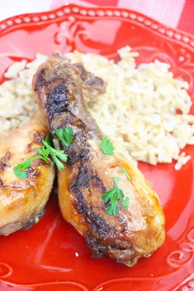 a close up of apple maple chicken legs and rice on a red plate on a red and white checkered cloth
