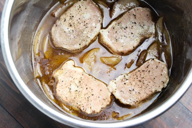 sliced apples coated with brown sugar and cinnamon, and pork chops in an instant pot on a brown table