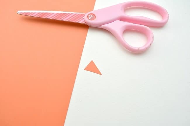 orange cardstock with a small triangle cut out of it and pink scissors on a white background