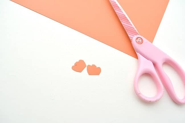 orange cardstock with two small turkey feet cut out of it and pink scissors on a white background