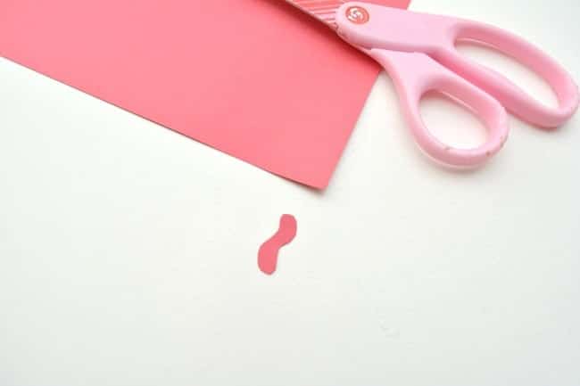 red cardstock with a small wattle cut out of it and pink scissors on a white background