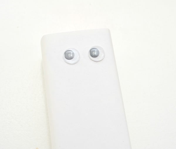 white paper wrapped around a juice box with two googly eyes on it on a white background