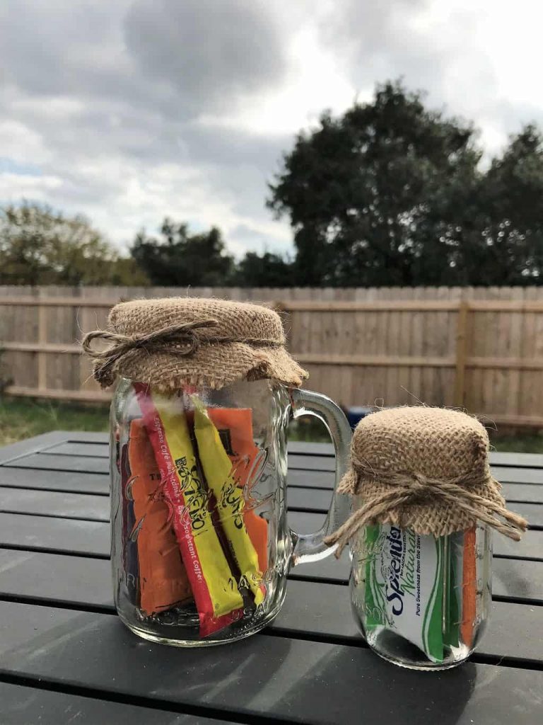 two mason jars filled with items for coffee drinkers topped with a burlap lid and tied with a brown yarn bow on a brown table outdoors