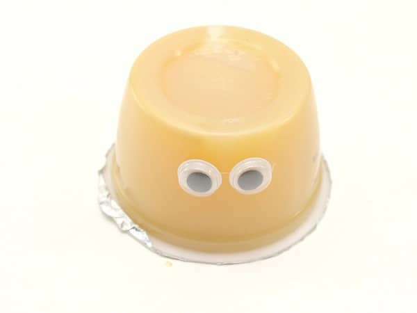 an upside down applesauce cup with googly eyes on it on a white background