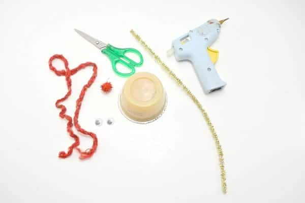 red yarn, red pom pom, google eyes, scissors, applesauce cup, gold pipe cleaner and hot glue gun on a white background