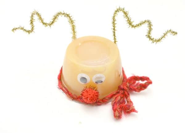 upside down applesauce cup decorated with googly eyes, red pom pom nose, red yarn scarf, and gold pipe cleaner antlers on a white background