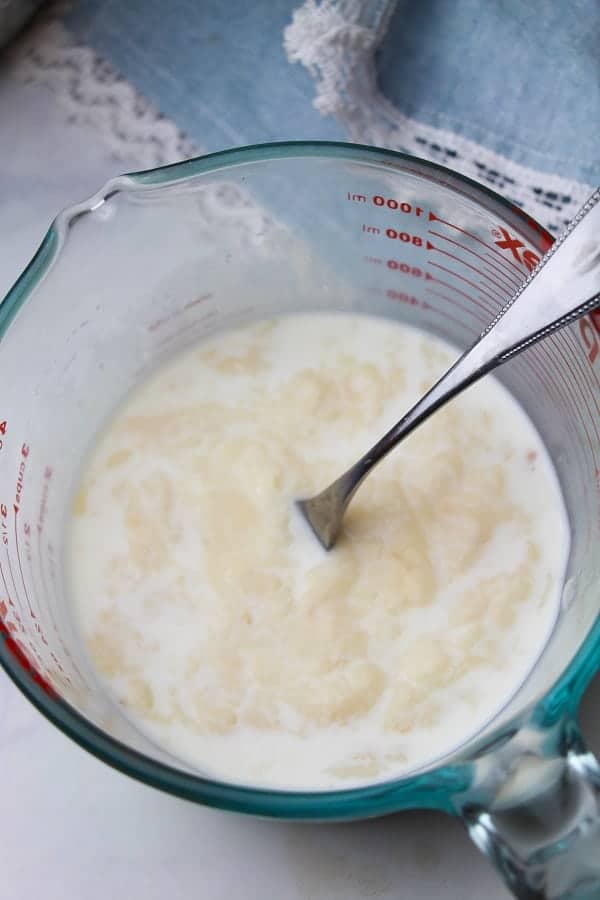 cream of chicken soup and milk, and a fork, in a glass measuring cup on a white cloth